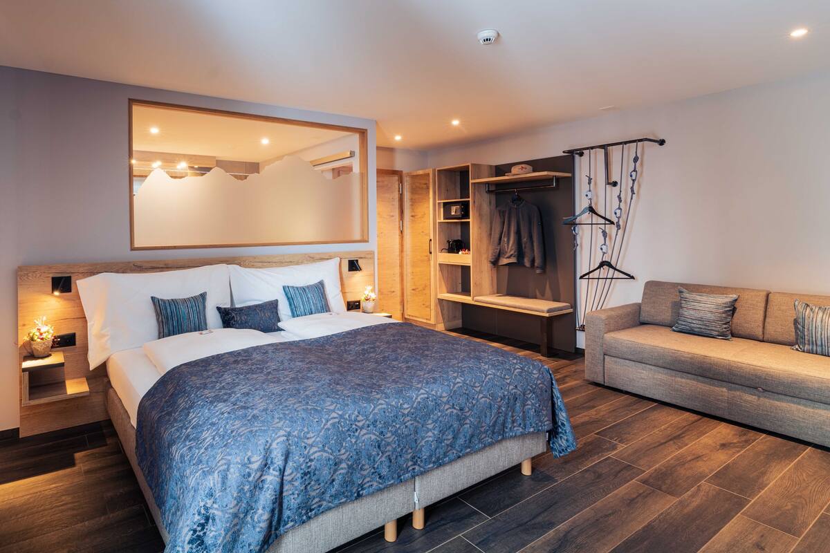 A modern bedroom with a large bed, a sofa, a wardrobe, and a mirror.