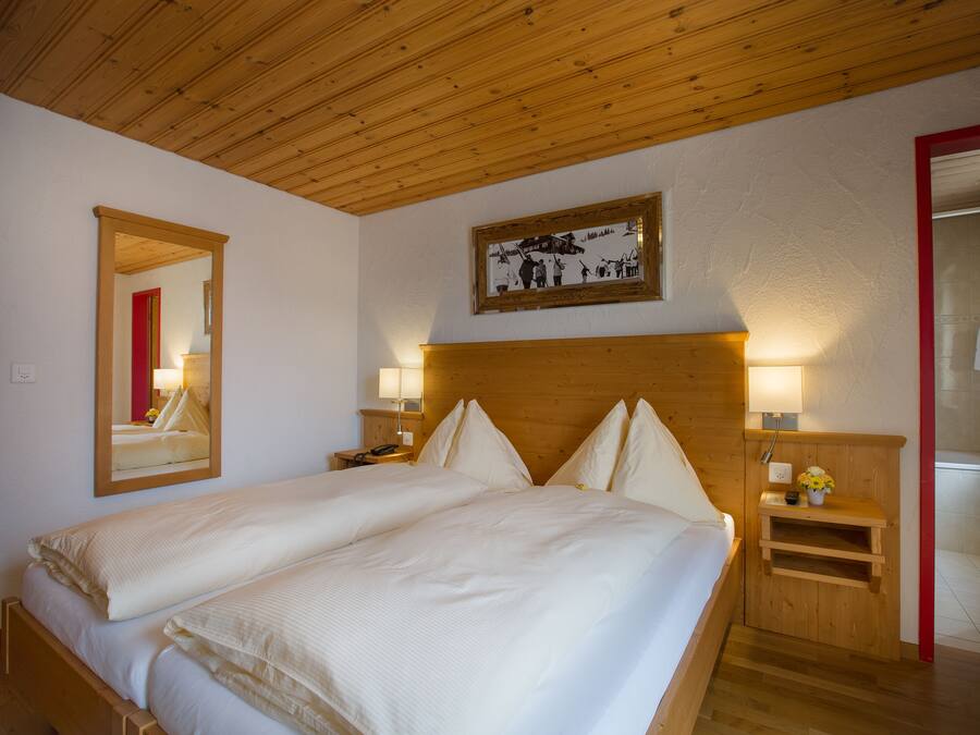 Een tweepersoonsbed met houten hoofdbord, nachtkastje met lamp, spiegel en een ingelijst kunstwerk aan de muur.