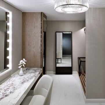 A modern bathroom with a vanity, mirror with lights, a chandelier, and a shower area.