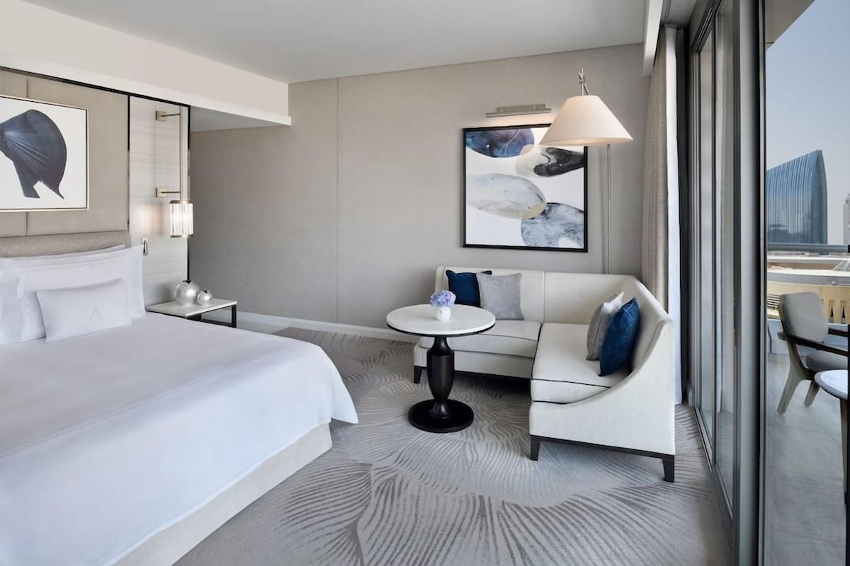 A modern hotel room with a large bed, a sofa, a small round table, and a city view.