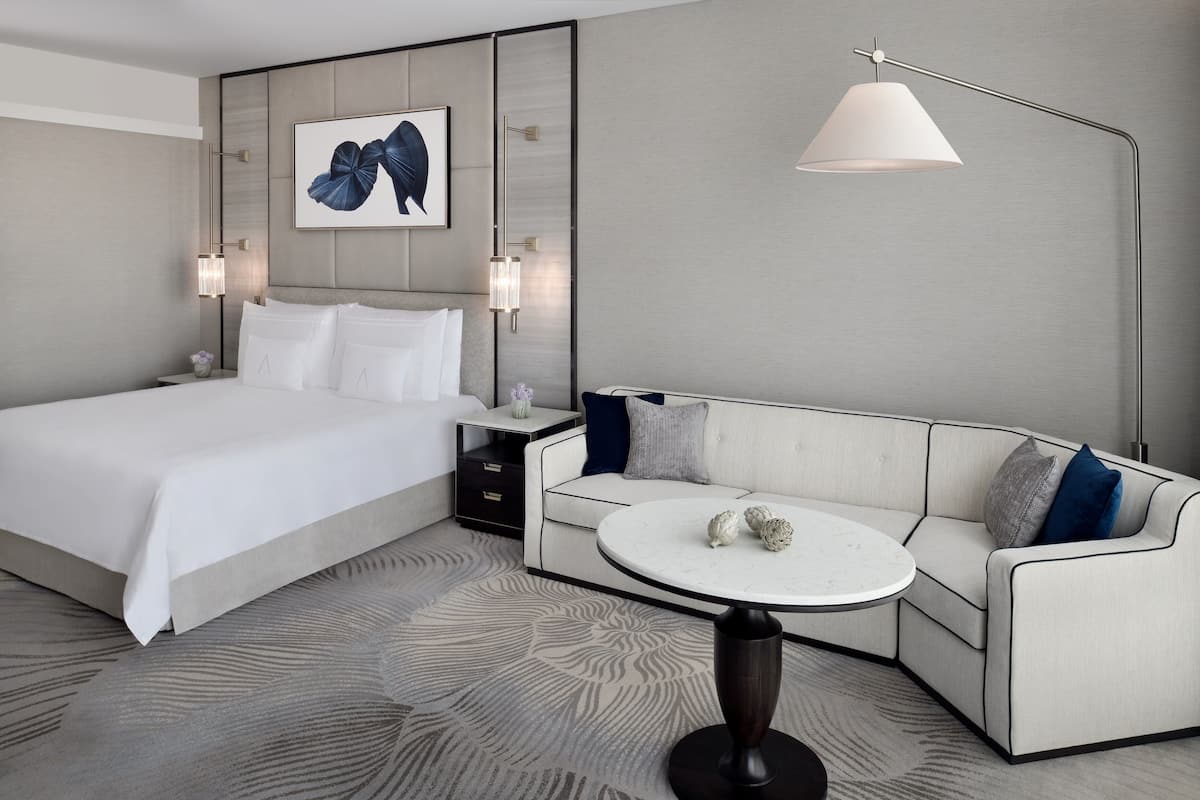 Moderni hotellihuone, jossa on suuri sänky, sohva, pyöreä sohvapöytä ja seinään kiinnitetty valaisin.