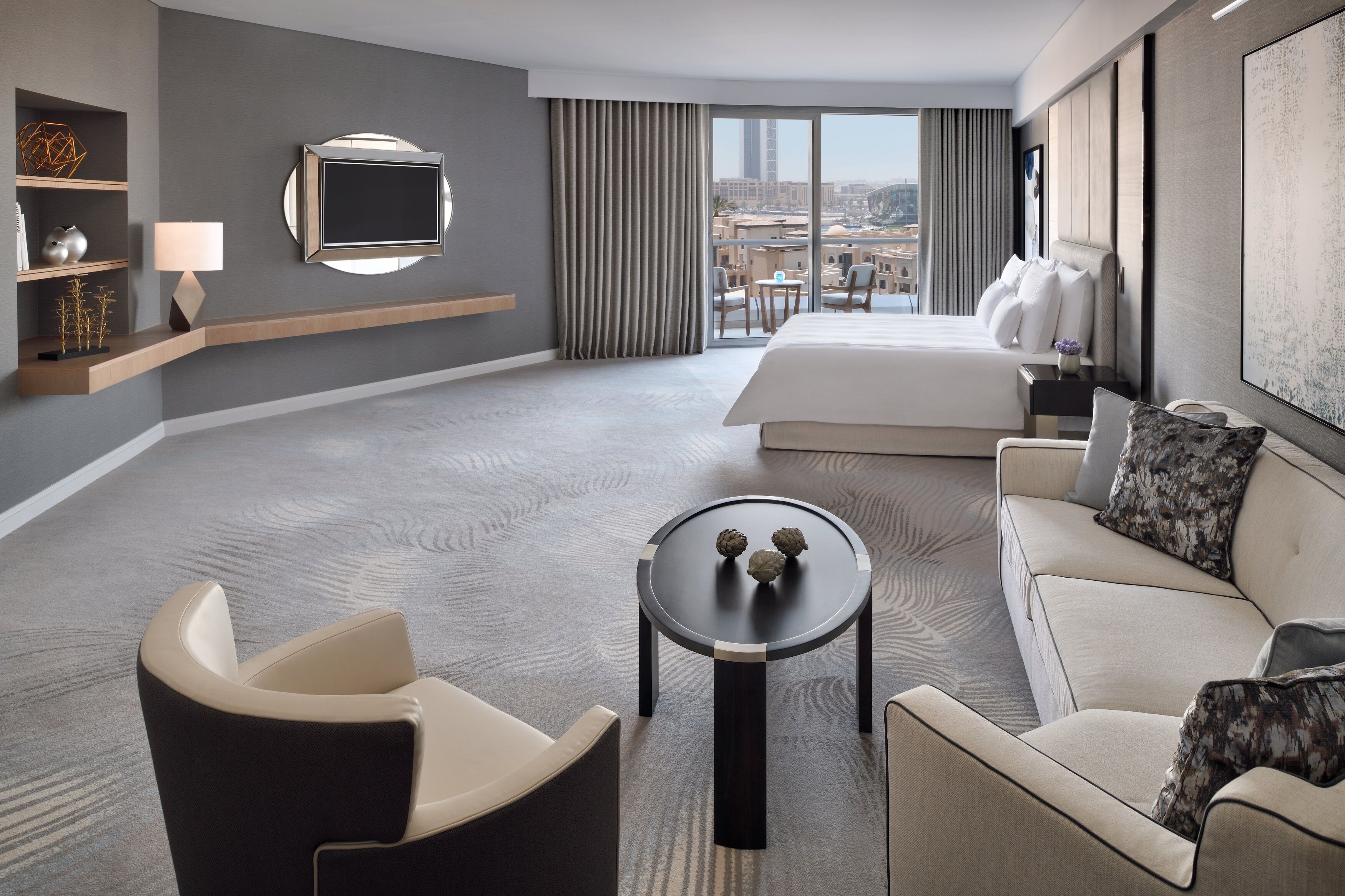 Une chambre d’hôtel moderne, dotée d’un grand lit, d’un canapé, d’une petite table et d’un téléviseur fixé au mur.