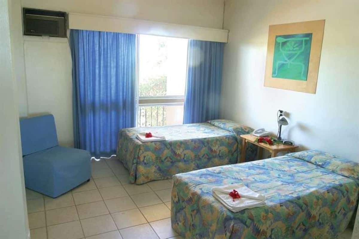 A room with two beds, a chair, a desk with a phone, and a window with curtains.