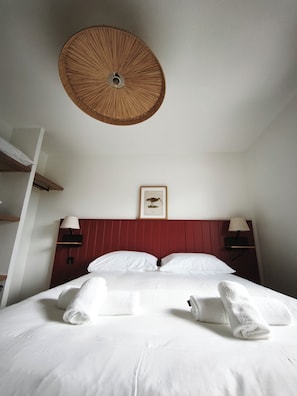 A hotel room with a bed, white linens, a red headboard, two bedside lamps, a wall-mounted picture, and a ceiling fan. - Hotel All Suites Le Teich (Le Teich)