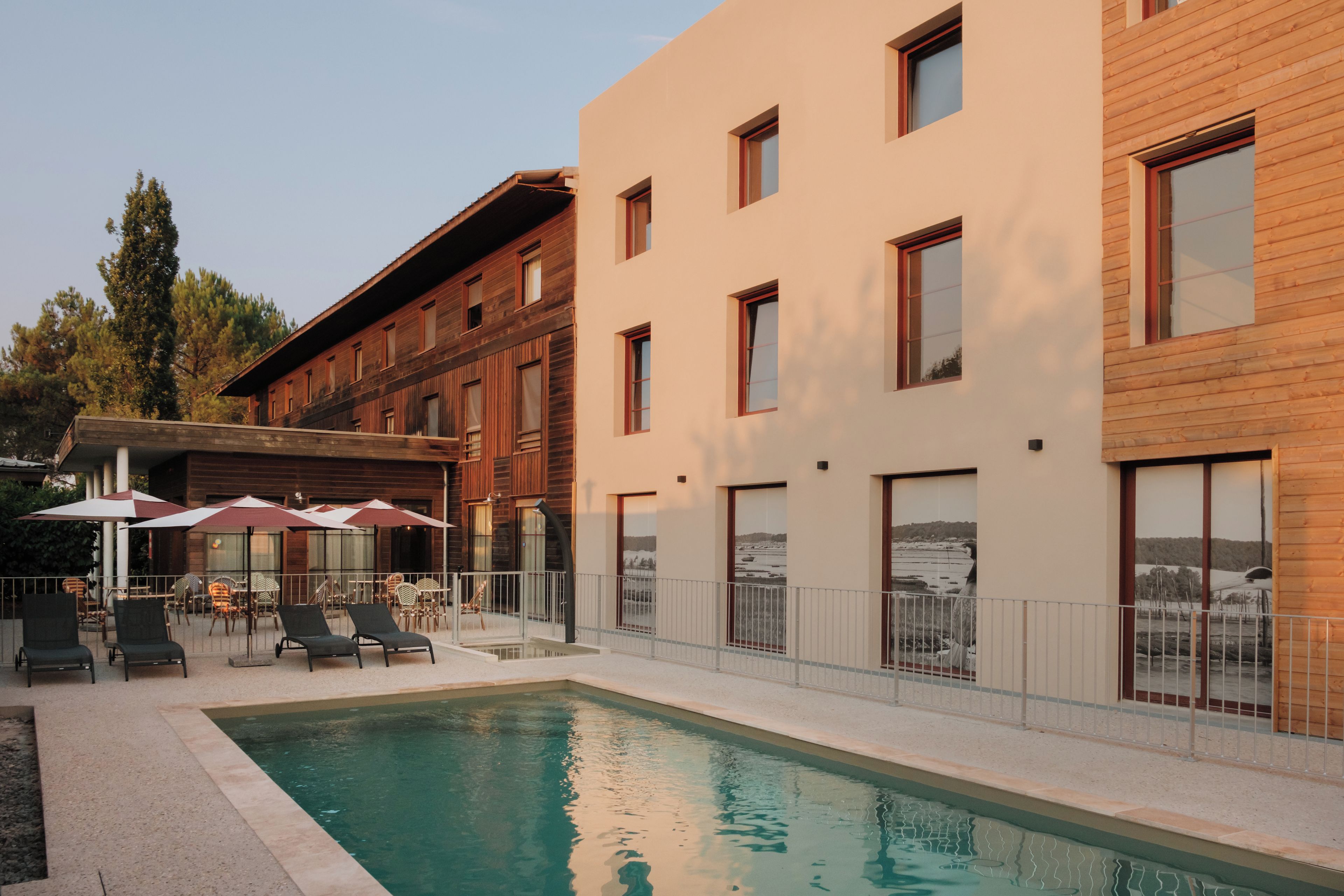 A pool area with lounge chairs and umbrellas, a building with multiple windows, and a view of a landscape.