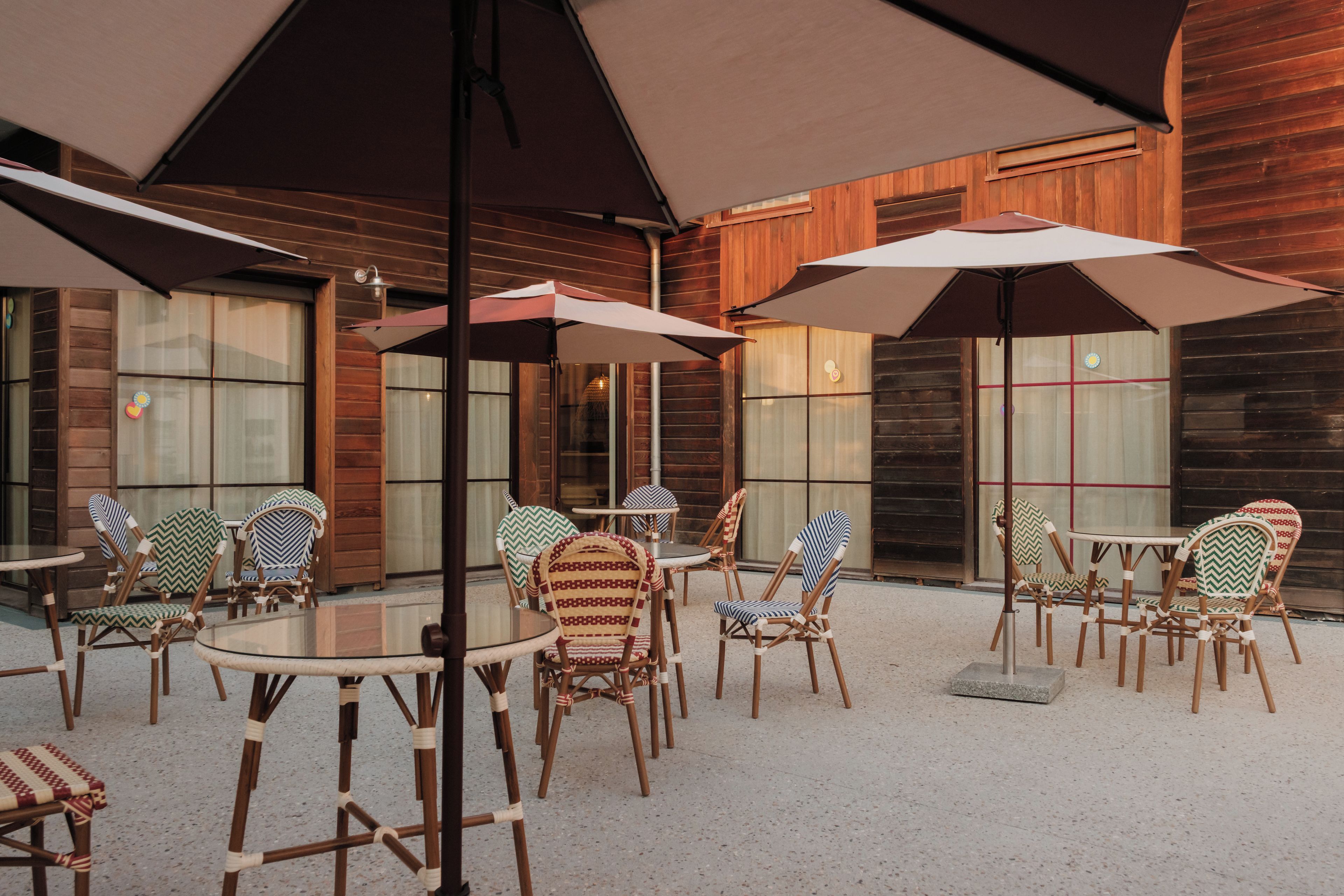 Un espace extérieur aménagé avec des tables et des chaises, des parasols et une façade en bois.