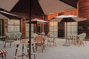 An outdoor seating area with tables and chairs, umbrellas, and a wooden building facade. - greet hôtel Le Teich Bassin d'Arcachon (Le Teich)