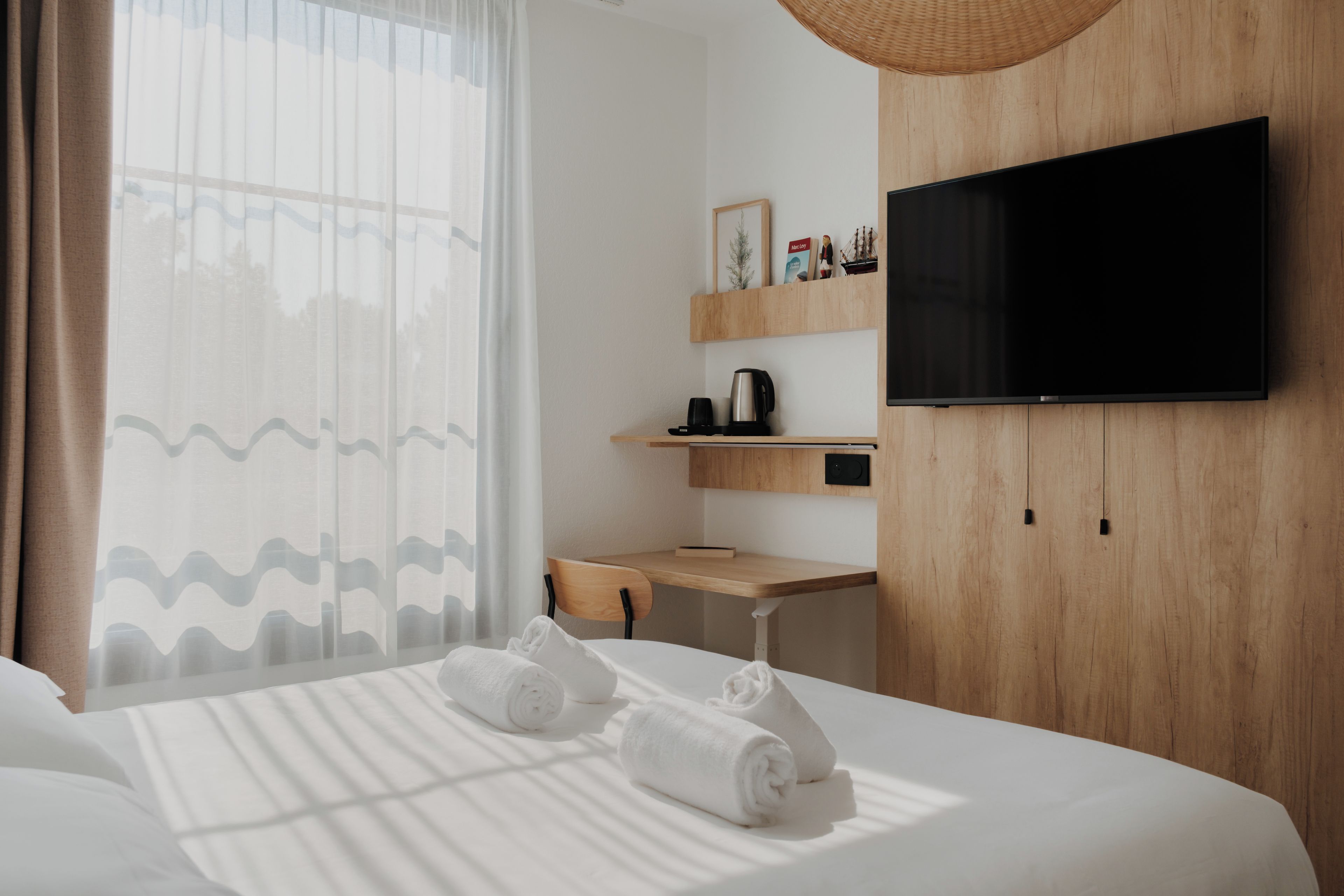 A hotel room with a bed, a desk, a television, and a window with curtains.