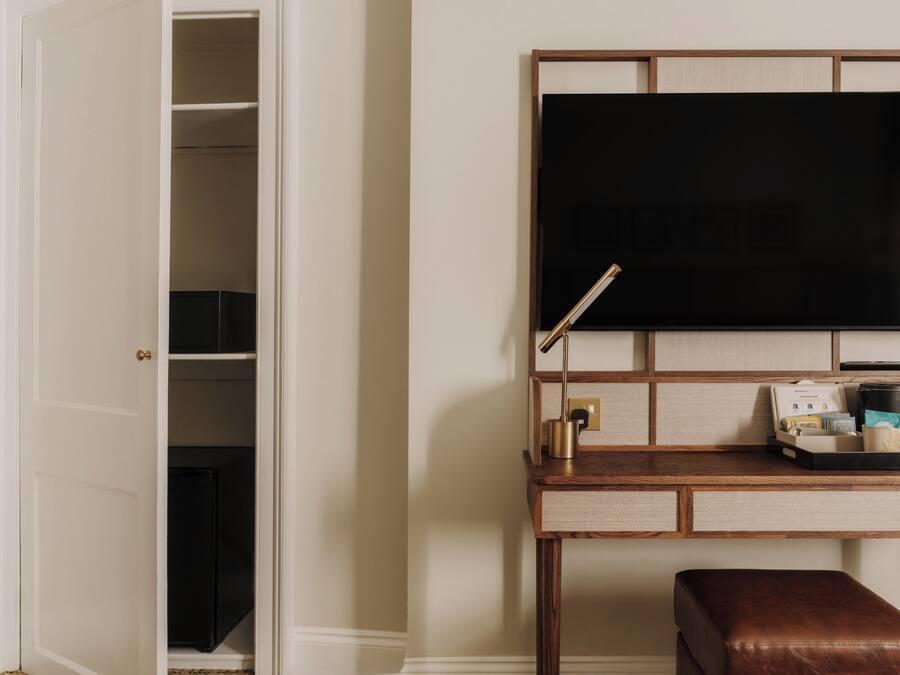 Habitación de hotel con escritorio, televisor de pantalla plana, cafetera y una banca.