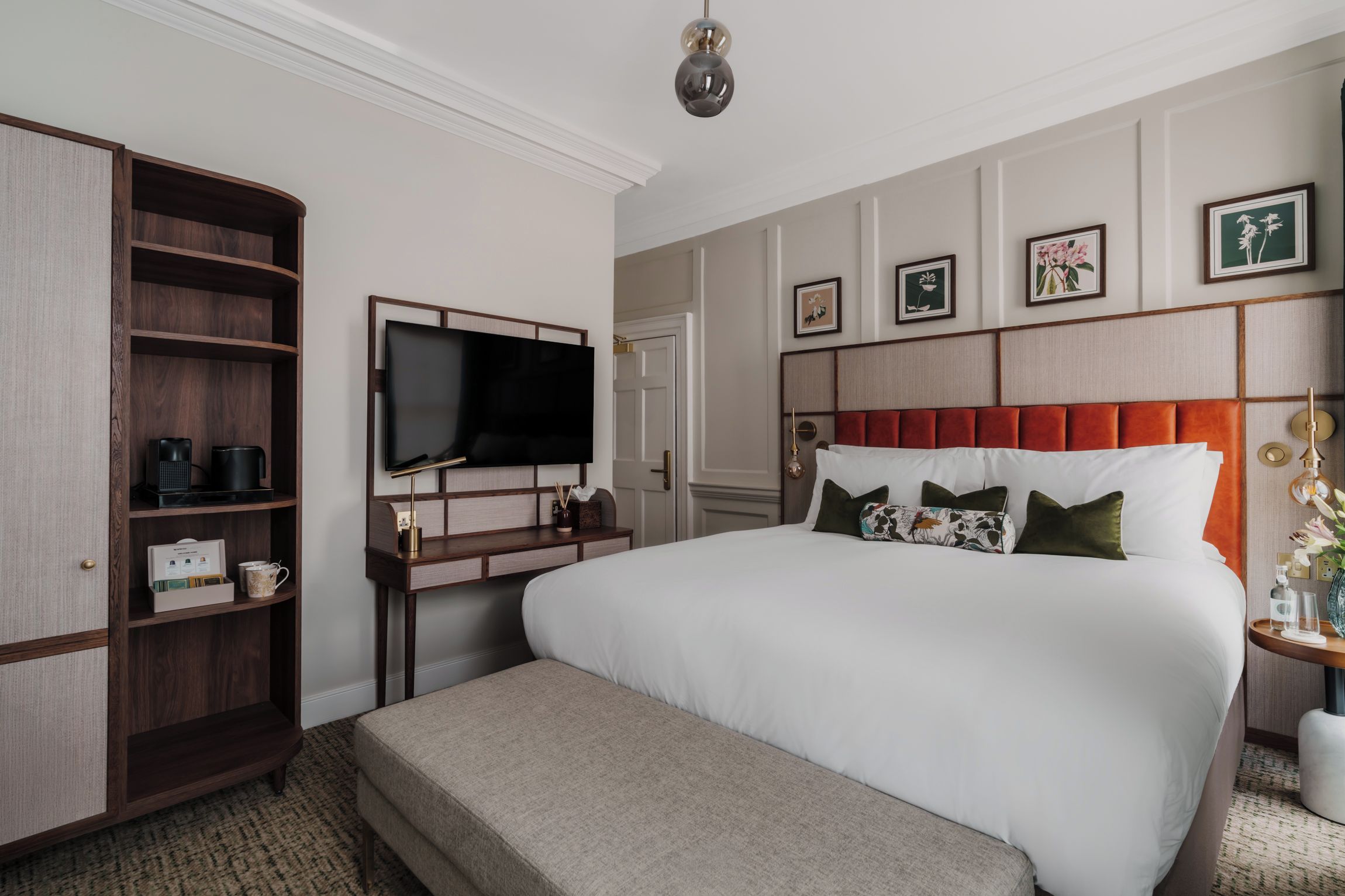 Habitación de hotel con una cama grande, un escritorio con televisor de pantalla plana, un armario y una mesita de noche con lámpara.