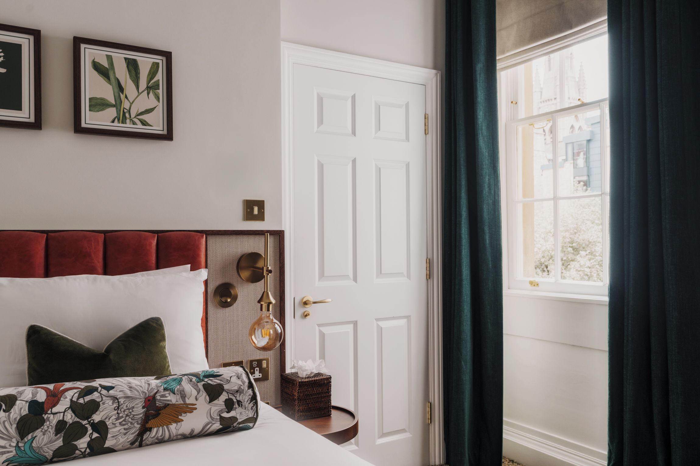 A bedroom with a bed, a bedside table, a door, and a window with curtains.