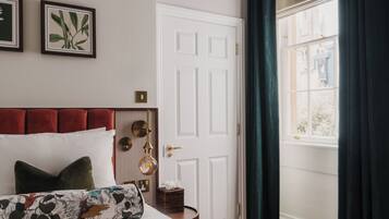 A bedroom with a bed, a bedside table, a door, and a window with curtains.