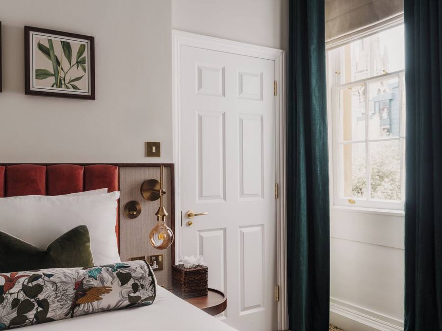A bedroom with a bed, a bedside table, a door, and a window with curtains.