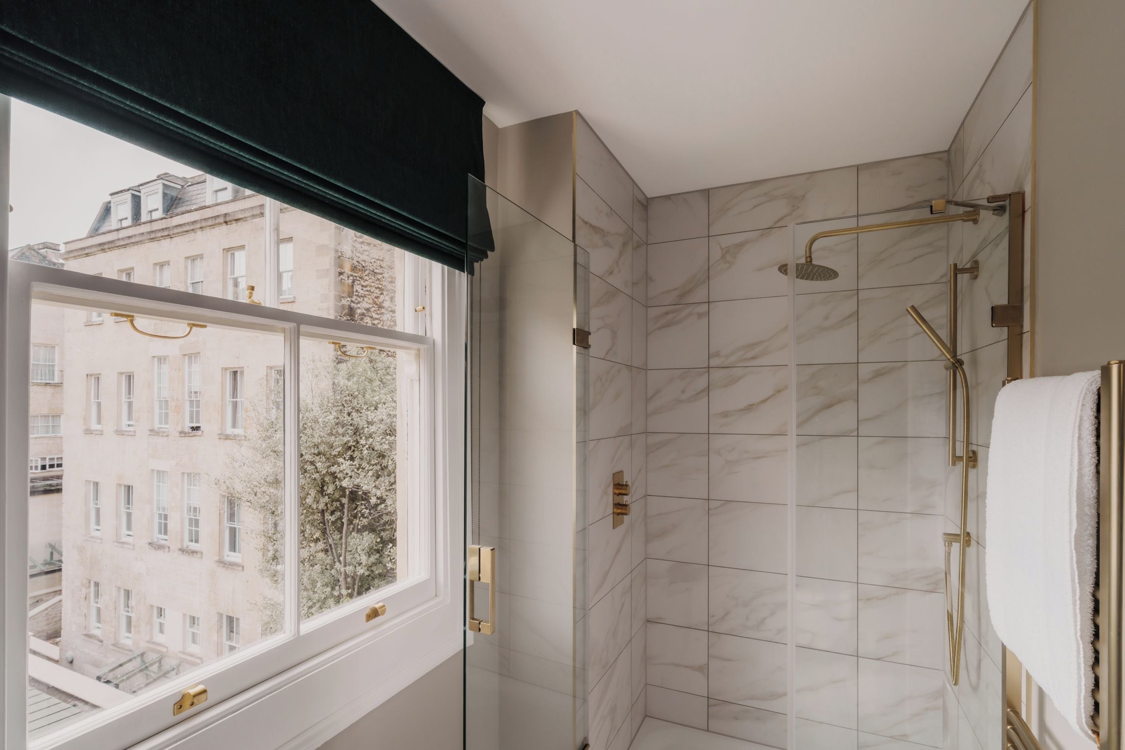 Een moderne badkamer met een douche, een raam en uitzicht op gebouwen.