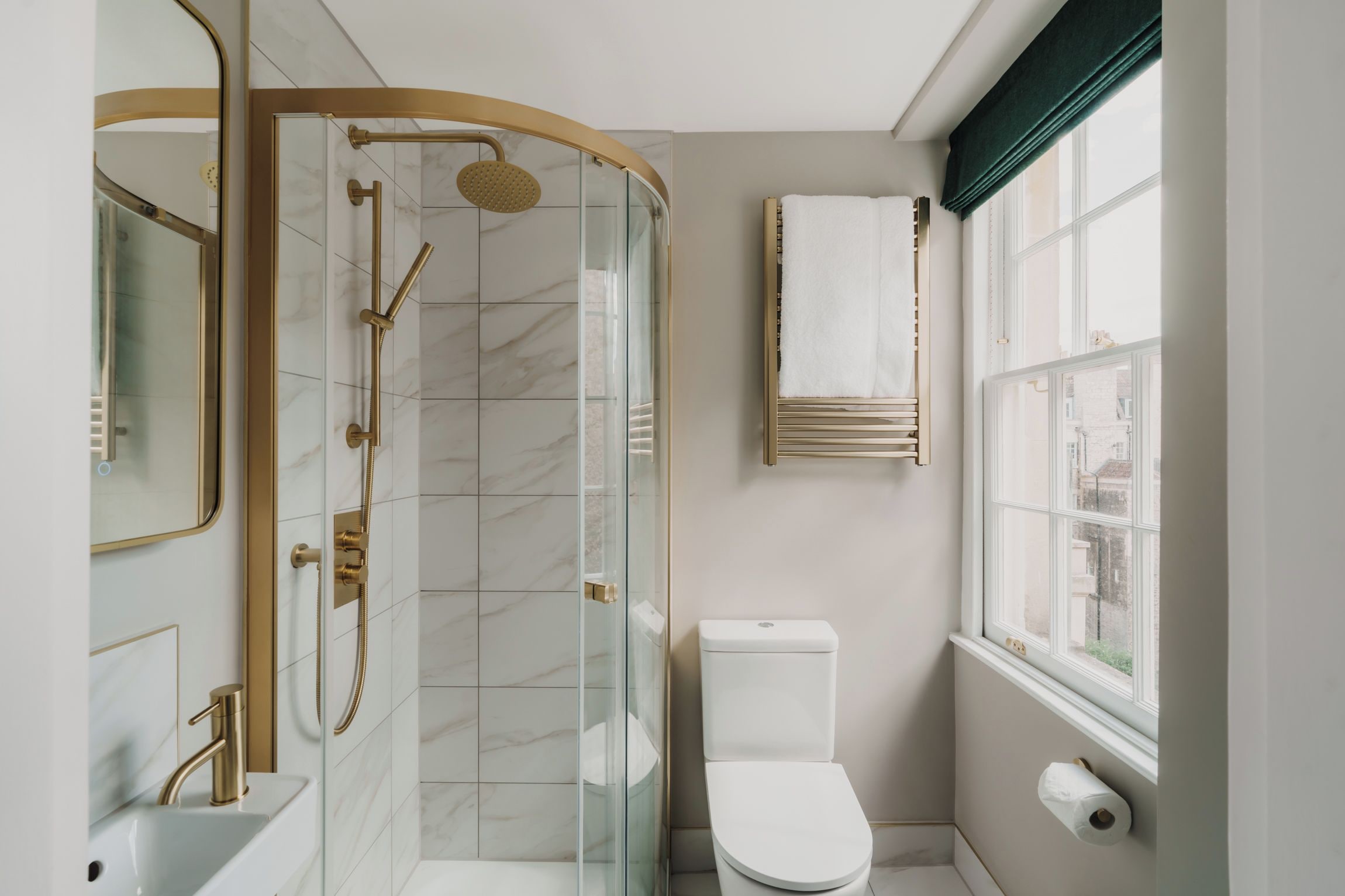 A modern bathroom with a glass-enclosed shower, a white toilet, and a sink with a gold faucet.