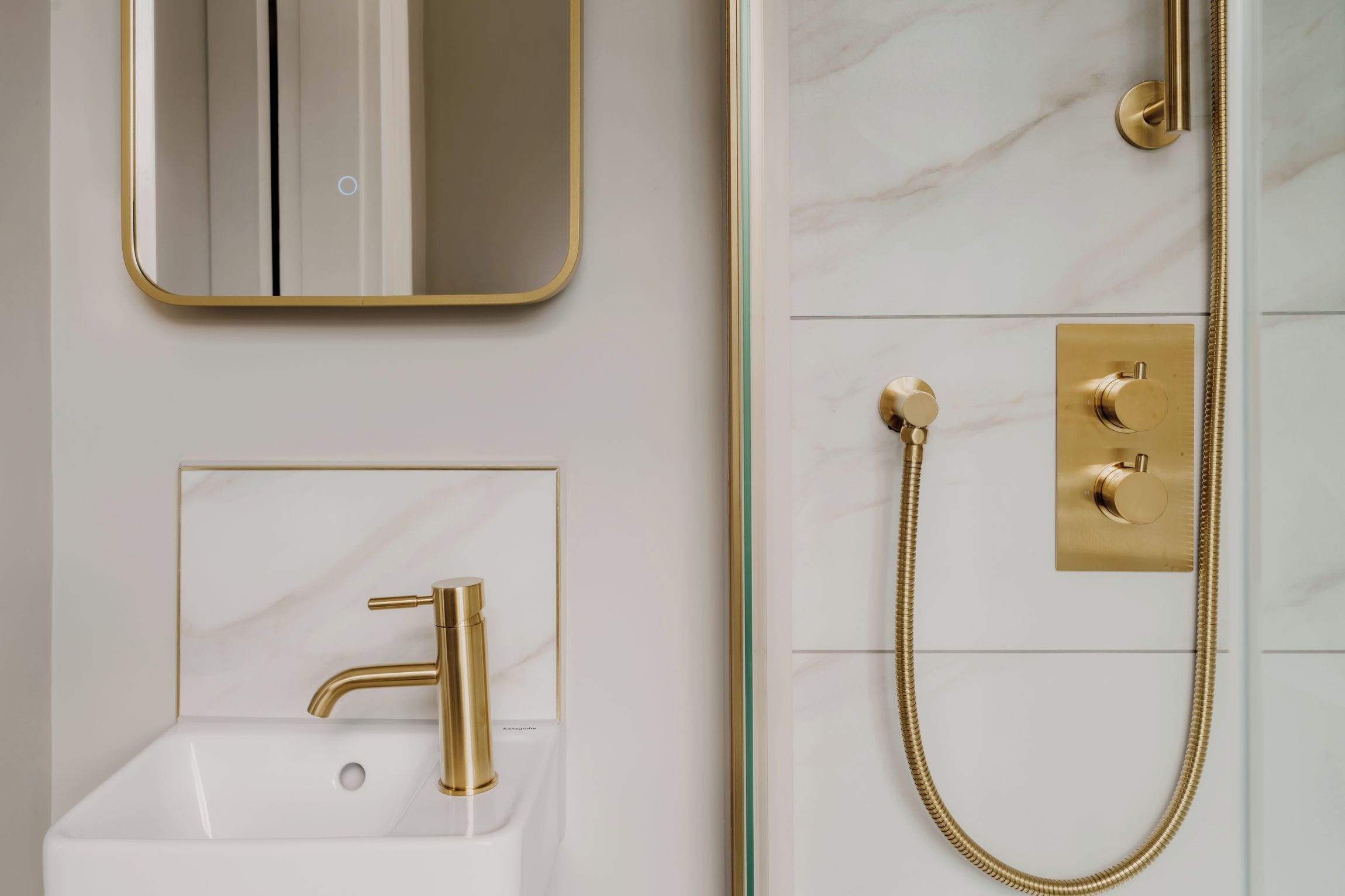Un baño con grifo dorado, cabezal de ducha dorado y manguera de ducha con matices dorados.