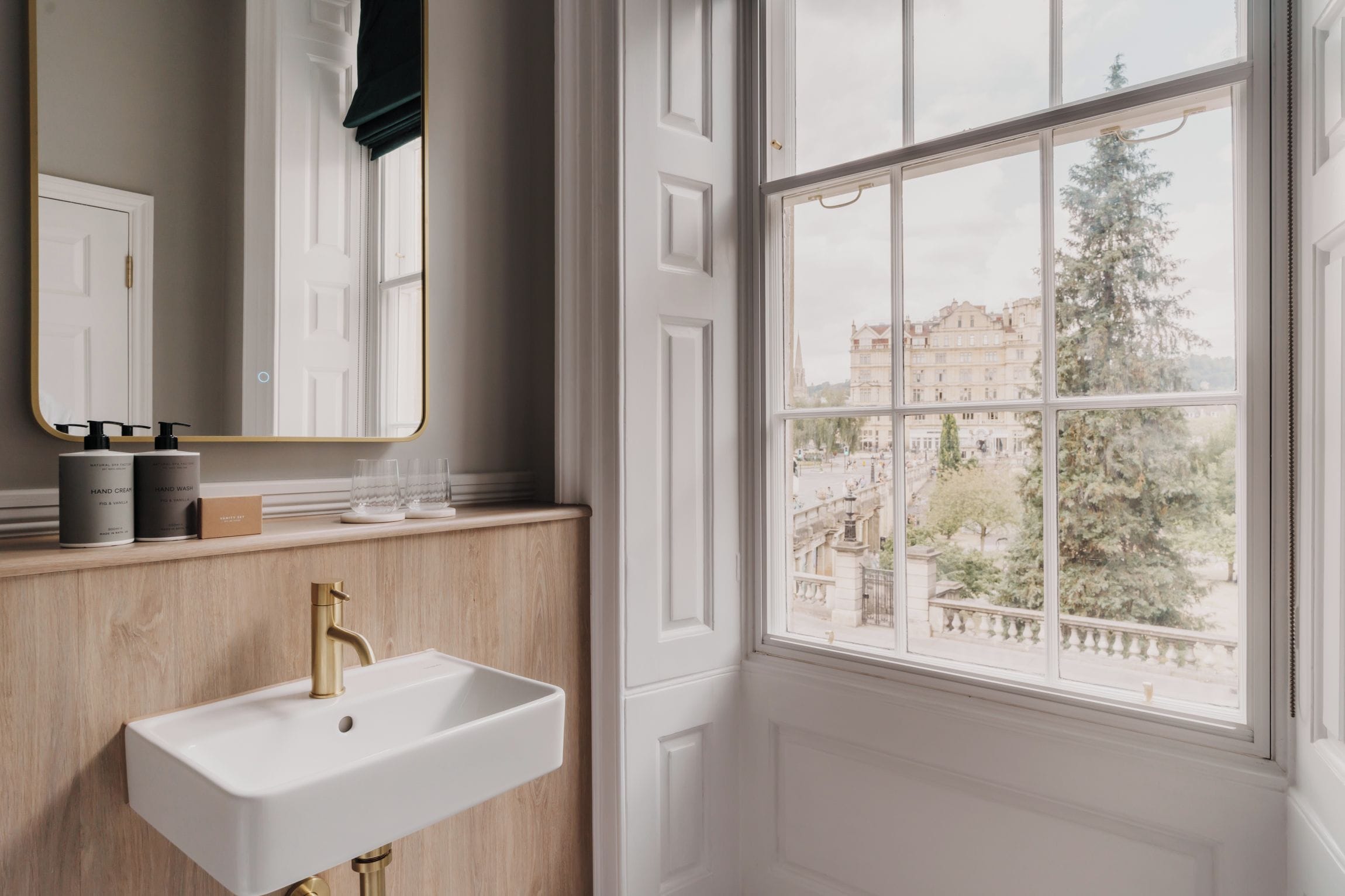 A bathroom with a white sink, a mirror, and a window with a view of buildings and trees.