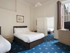 A hotel room with a large bed, a bedside table, a dresser, a television, and a door leading to another room. - Parade Hotel Bath (Bath)