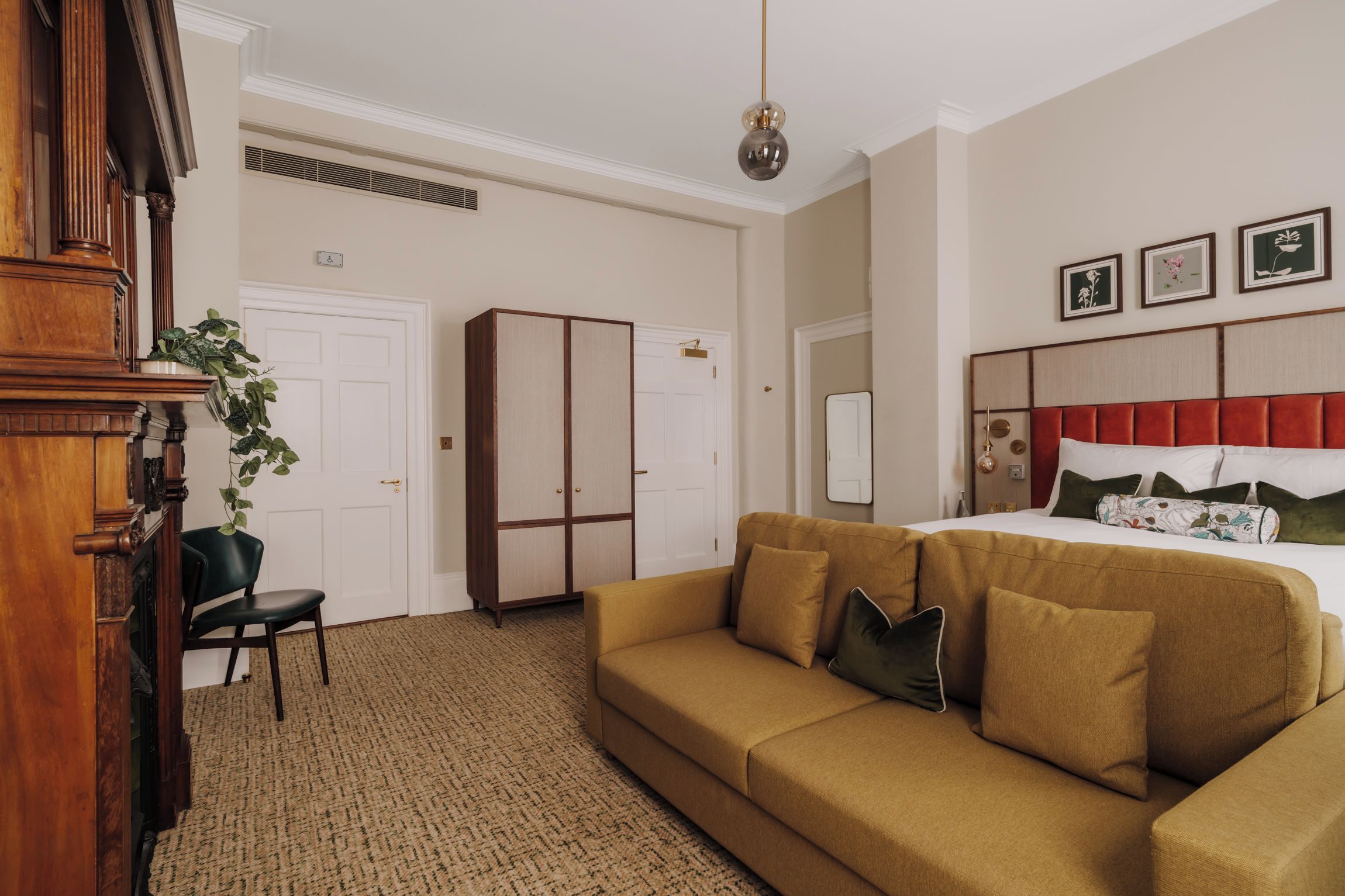 A hotel room with a large bed, a sofa, a desk, and a plant.