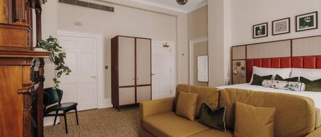 A hotel room with a large bed, a sofa, a desk, and a plant.