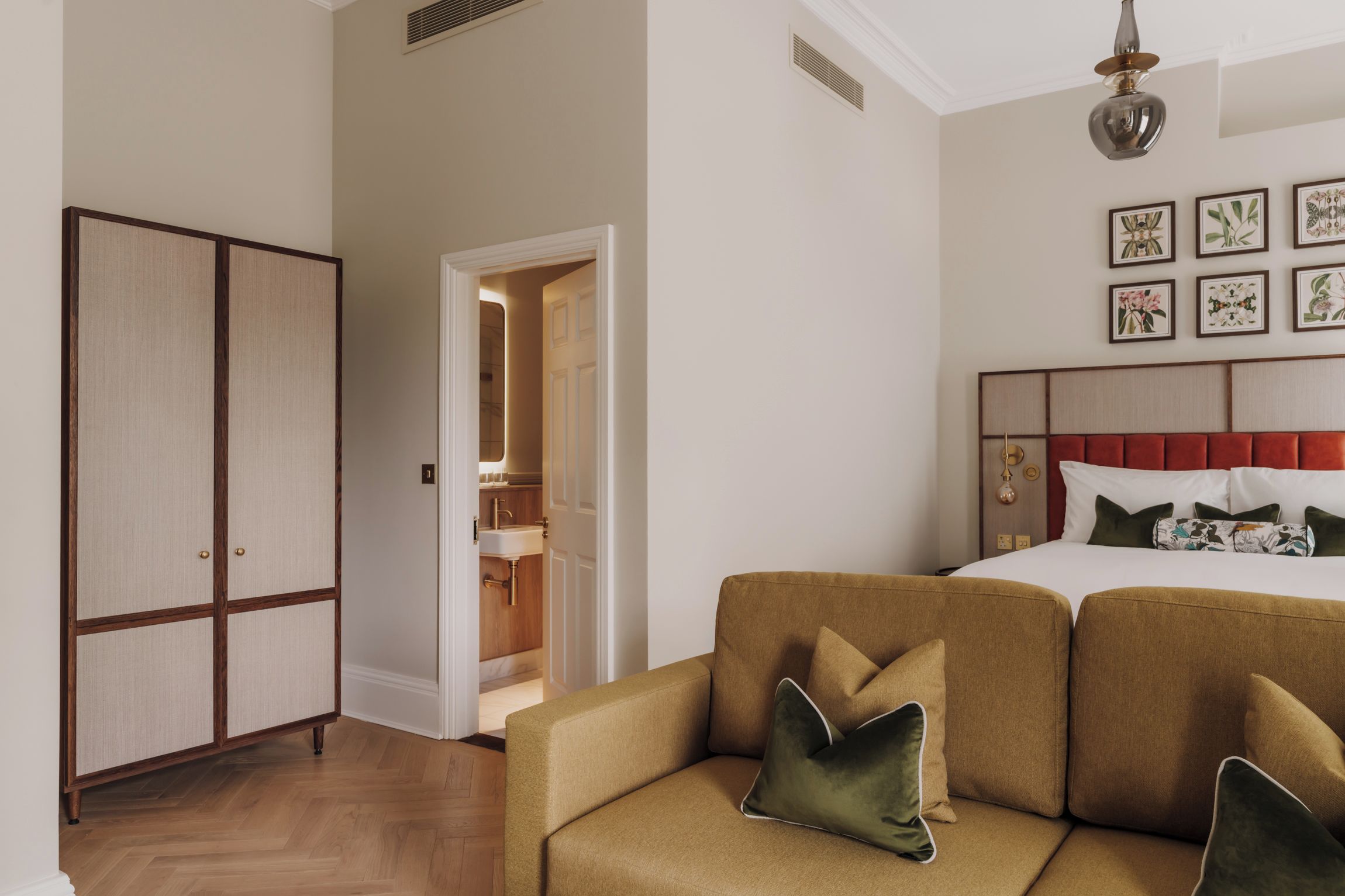 Habitación de hotel con cama, sofá, armario y baño visible a través de una puerta abierta.