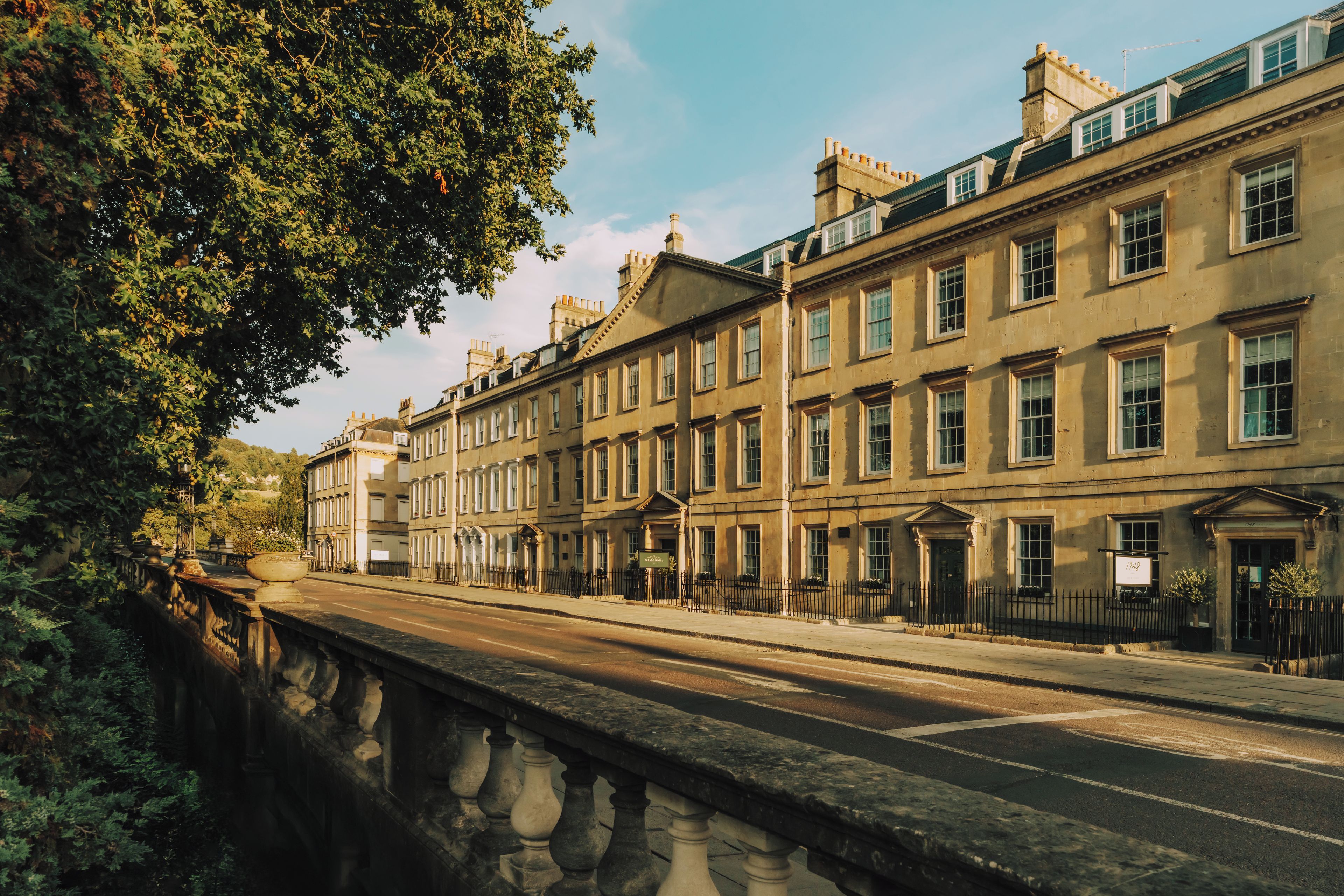 A row of historic buildings with uniform architecture, a stone bridge, and a clear sky.
