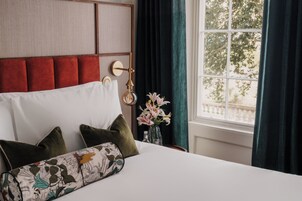 A hotel room with a bed, pillows, a nightstand, a lamp, and a window with curtains.