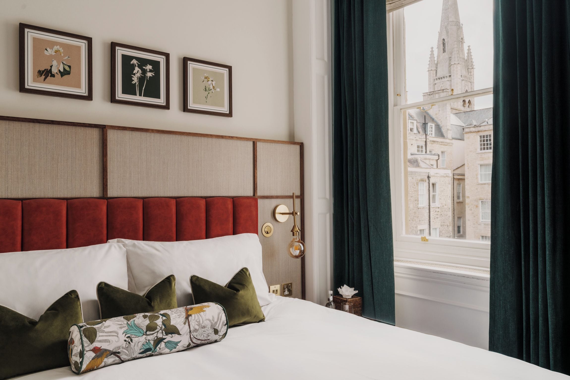 A hotel room with a bed, a headboard, a window with curtains, and three framed pictures on the wall.