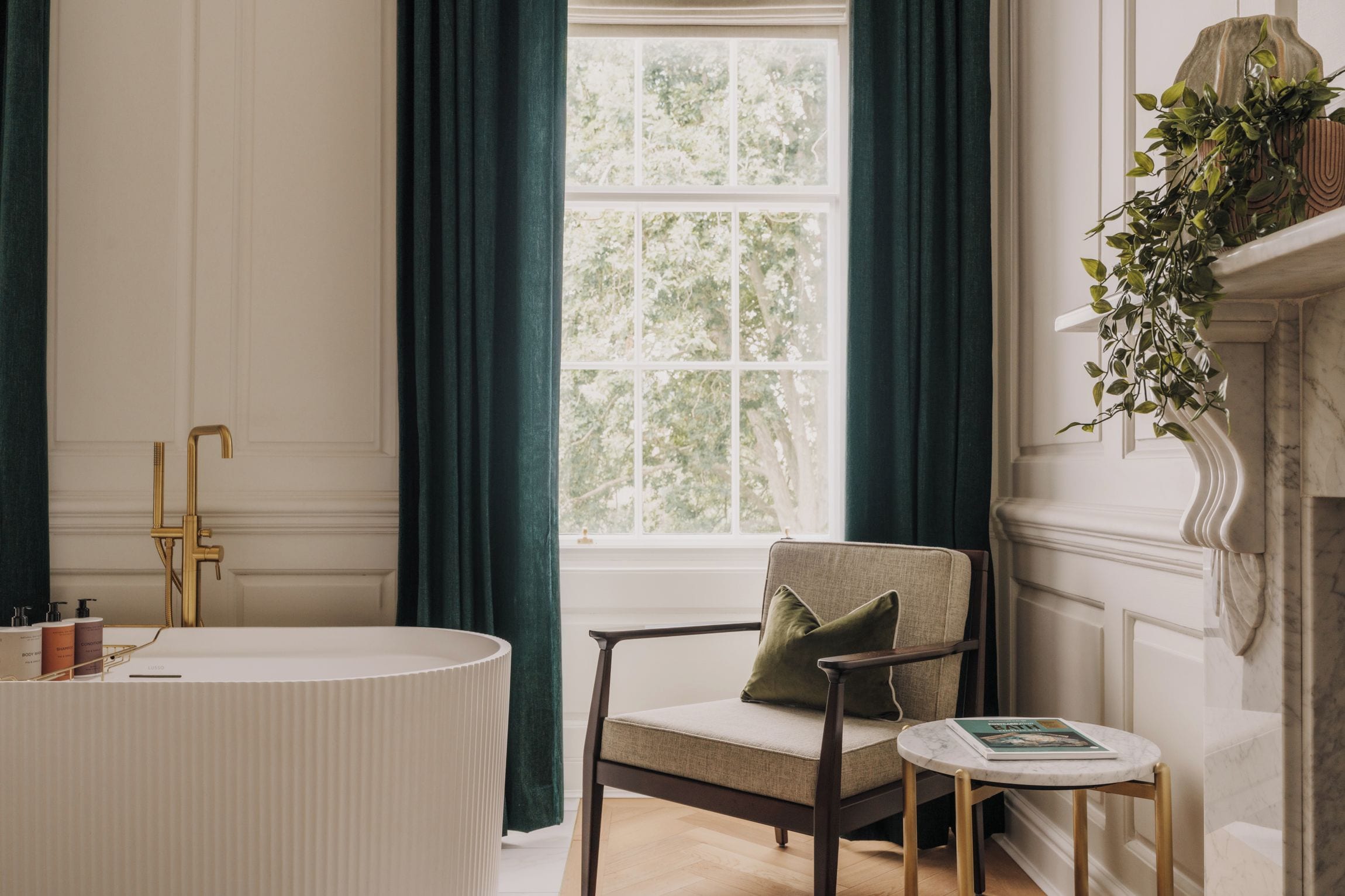 Ein Badezimmer mit einer freistehenden Badewanne, einem Sessel und einem kleinen Tisch mit einem Buch.