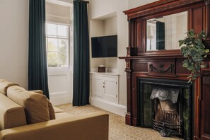 A living room with a sofa, a fireplace, a television, and a window with curtains. - Parade Hotel Bath (Bath)