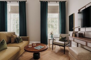 A well-lit living room with a sofa, armchairs, a coffee table, and a television. - Parade Hotel Bath (Bath)