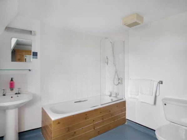 A bathroom with a wooden vanity, a sink, a toilet, and a glass-enclosed shower. - Parade Hotel Bath (Bath)