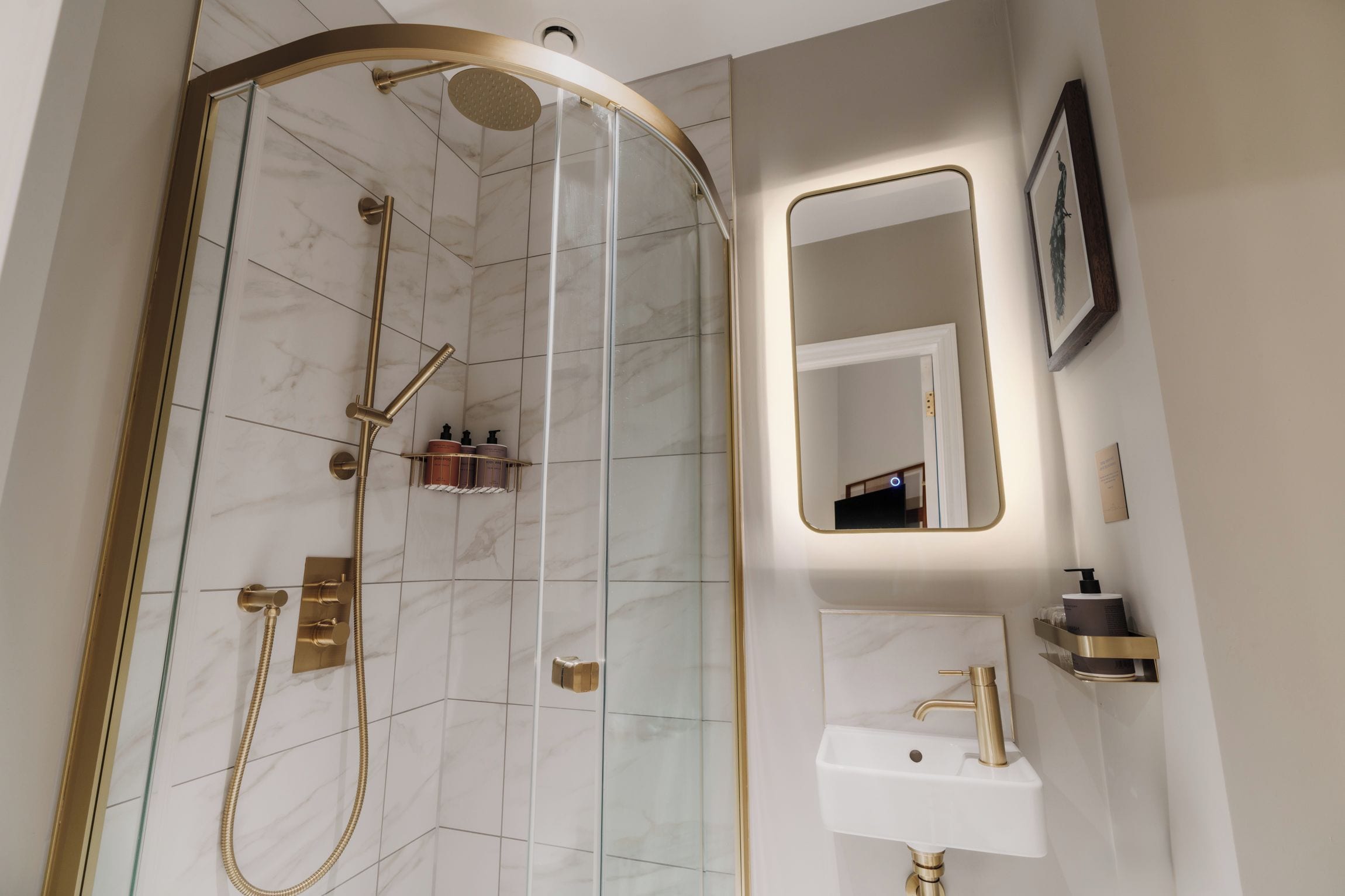 A modern bathroom with a glass-enclosed shower, a gold-colored showerhead, and a white sink with a gold faucet.