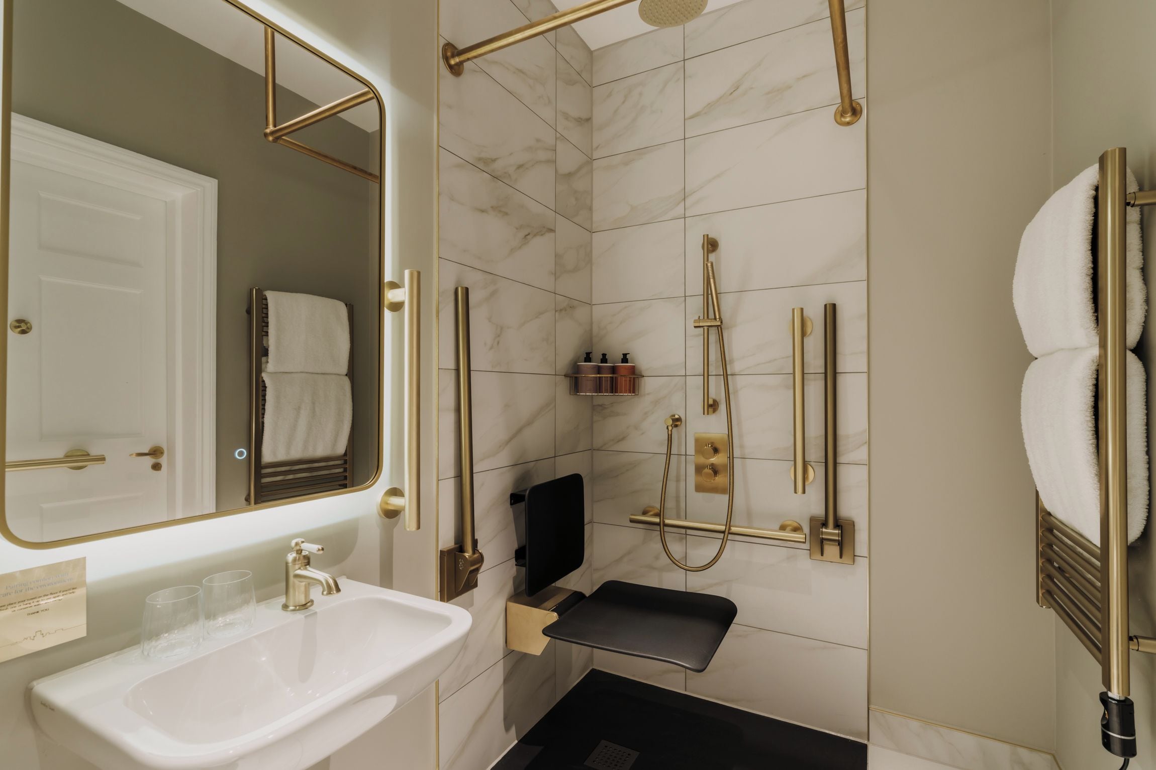 A modern bathroom with a white sink, a mirror, a shower with a handheld showerhead, and a towel rack.