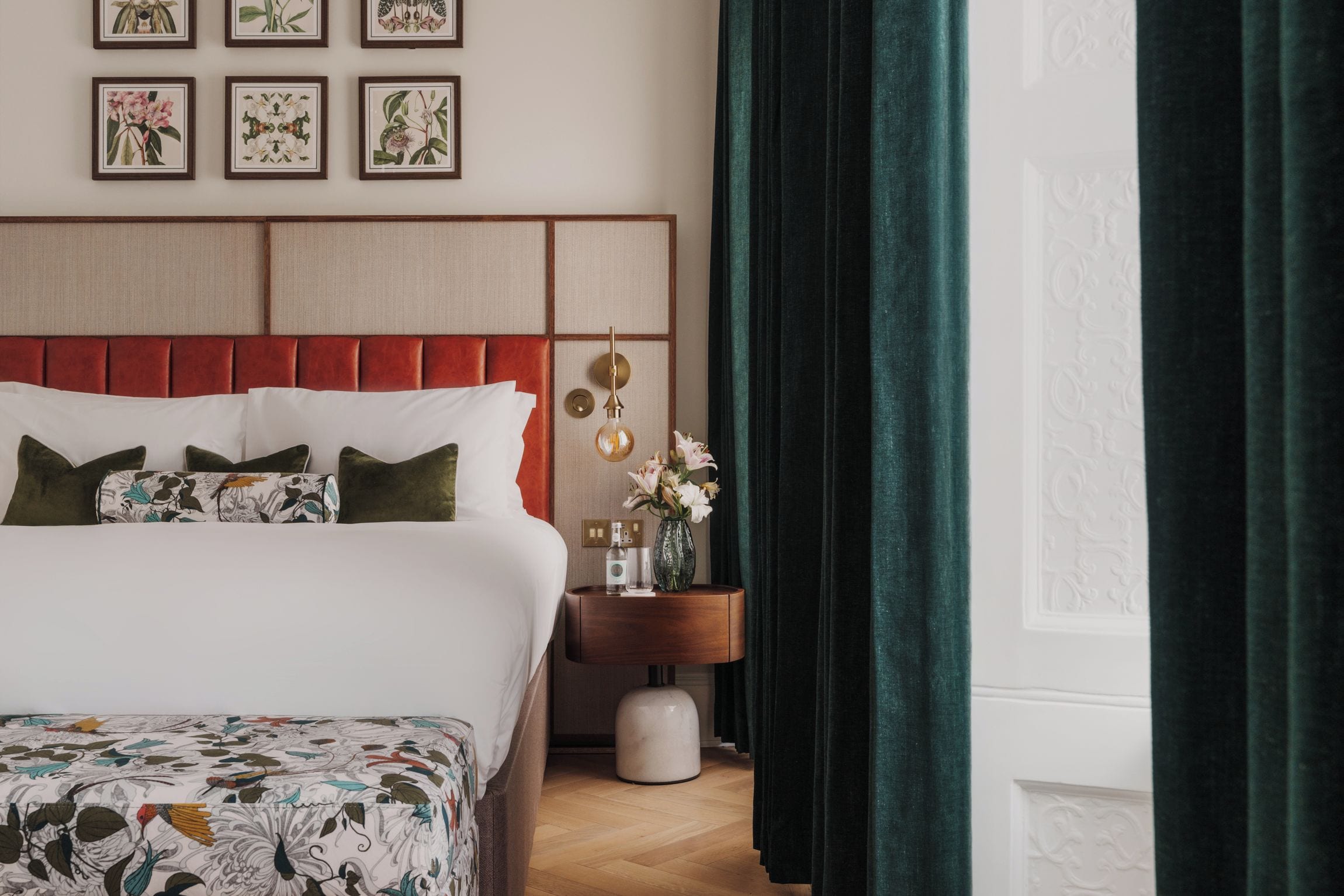 Ein Hotelzimmer mit Bett, Nachttisch, Blumenvase und einem Fenster mit Vorhängen.
