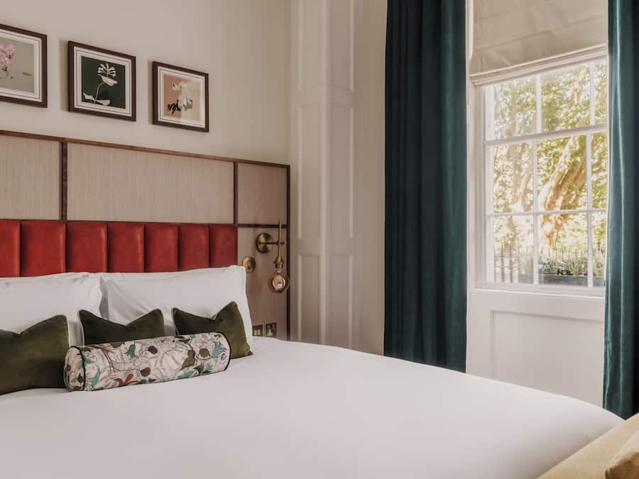Cama com cabeceira, almofadas e janela com cortinas.