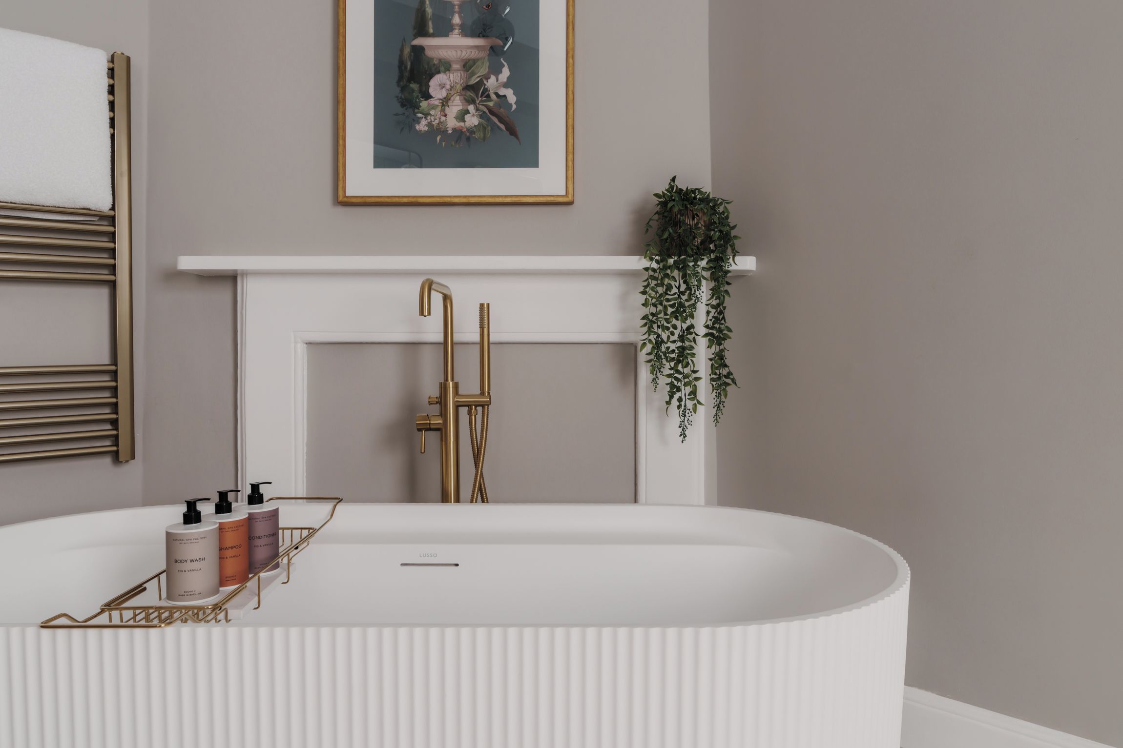 Un baño moderno con una bañera independiente, un cabezal de ducha dorado y un tocador blanco con artículos de aseo.