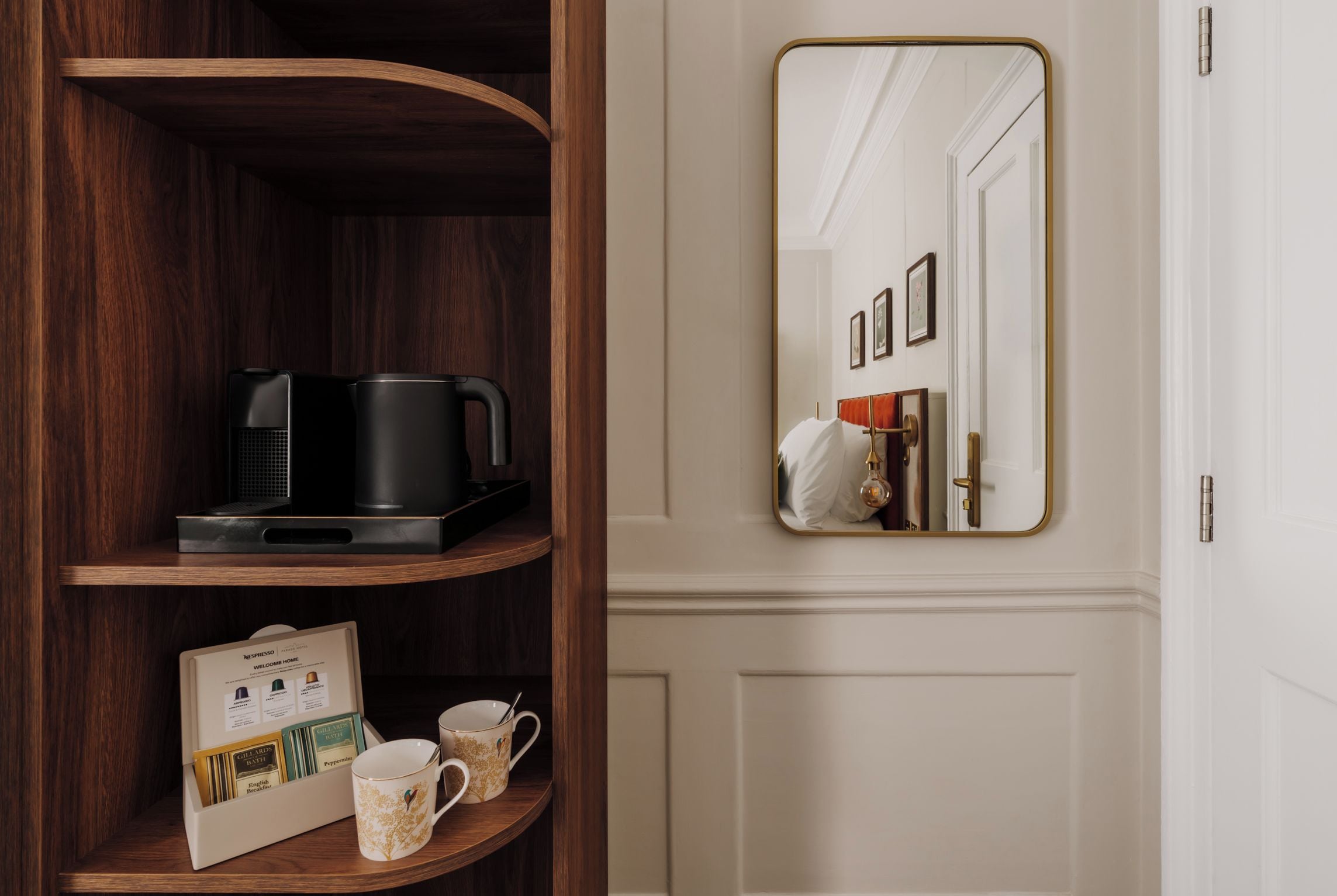 Une étagère en bois sur laquelle se trouvent une machine à café noire et une cafetière, une carte de bienvenue encadrée, ainsi que deux tasses à café.