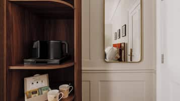 Une étagère en bois sur laquelle se trouvent une machine à café noire et une cafetière, une carte de bienvenue encadrée, ainsi que deux tasses à café.