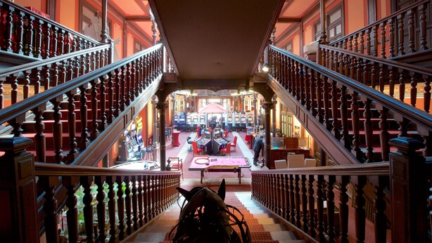 Una imponente escalera con barandillas ornamentales conduce a un área de recepción con mesa de billar y varias mesas de juego.