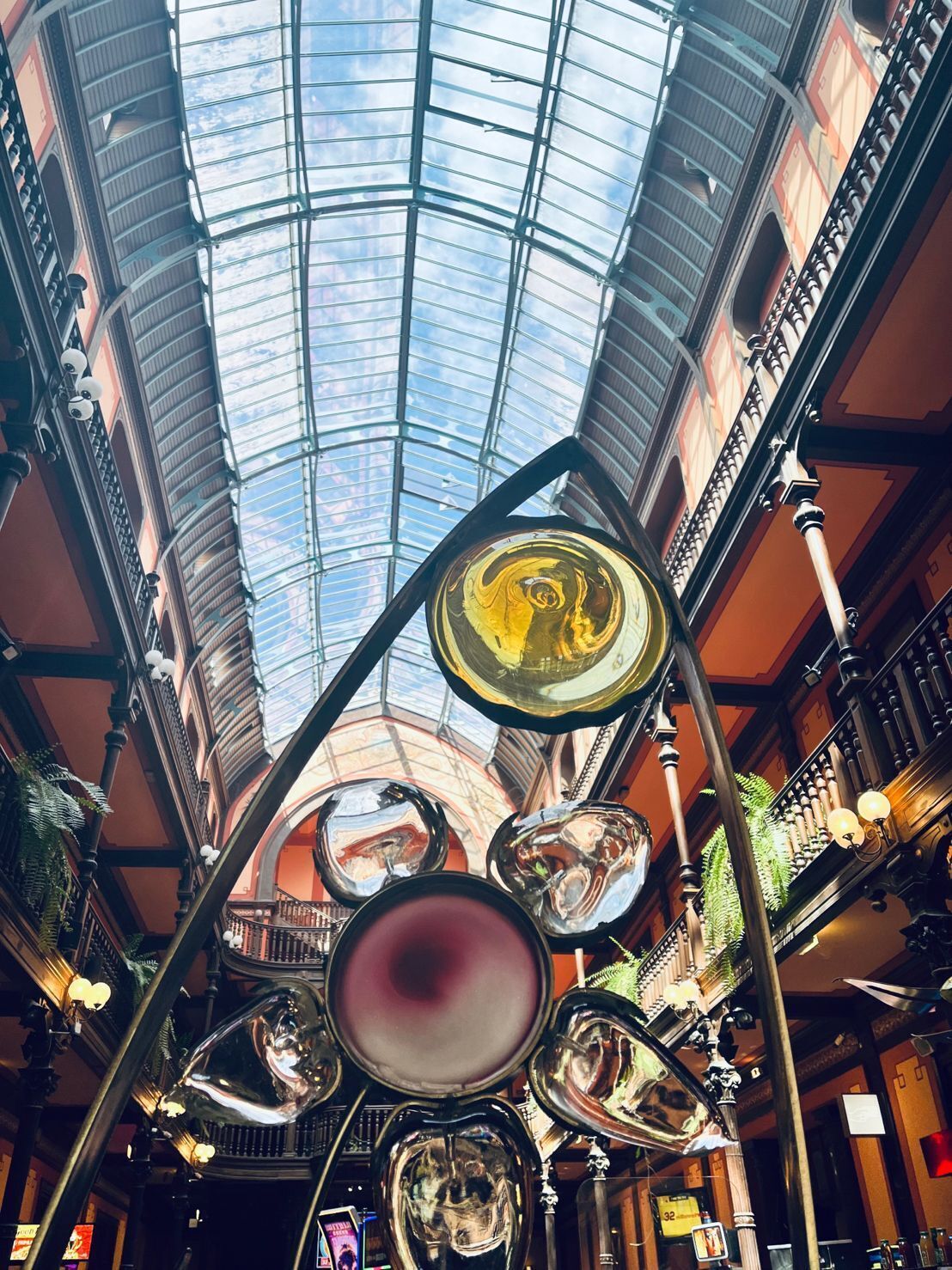 Eine Glasdecke mit Blick zum Himmel, eine Metallkonstruktion mit reflektierenden Oberflächen und aufwendige Geländer.