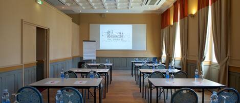 A conference room with tables, chairs, and a projector screen displaying text.