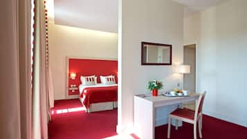 A hotel room with a red accent wall, a bed with white bedding, a desk with a chair, and a bedside table with a lamp and a vase of flowers.