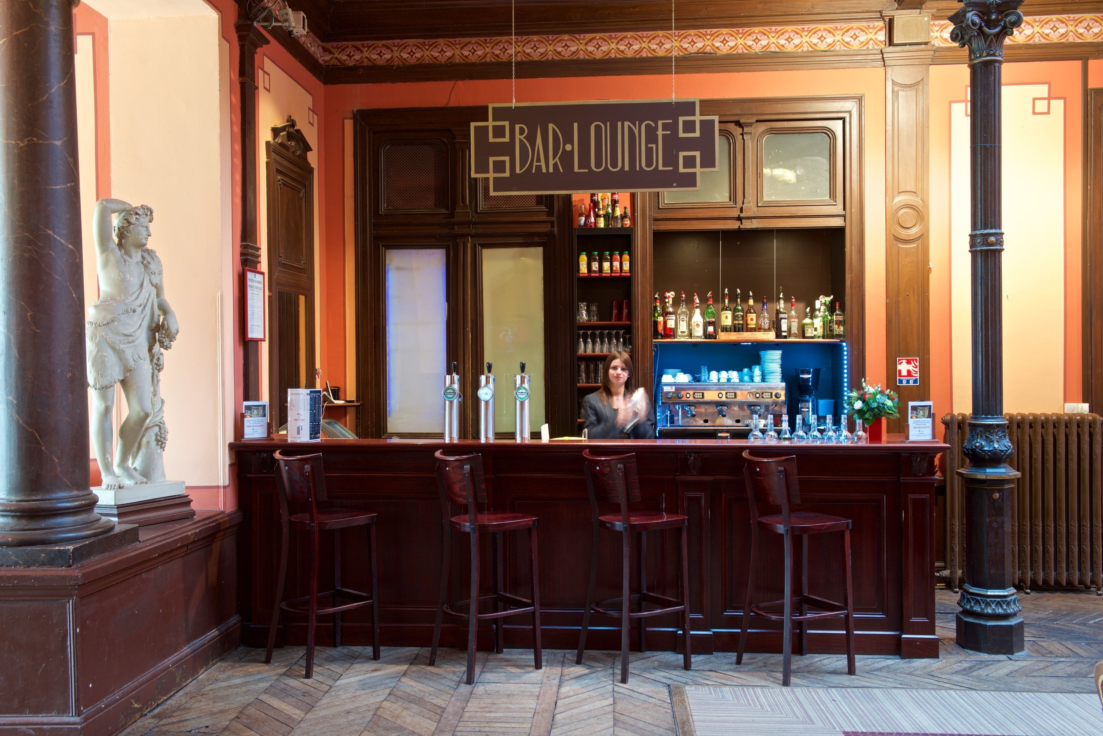 A bar/lounge area with a wooden counter, bar stools, and a statue on the left.