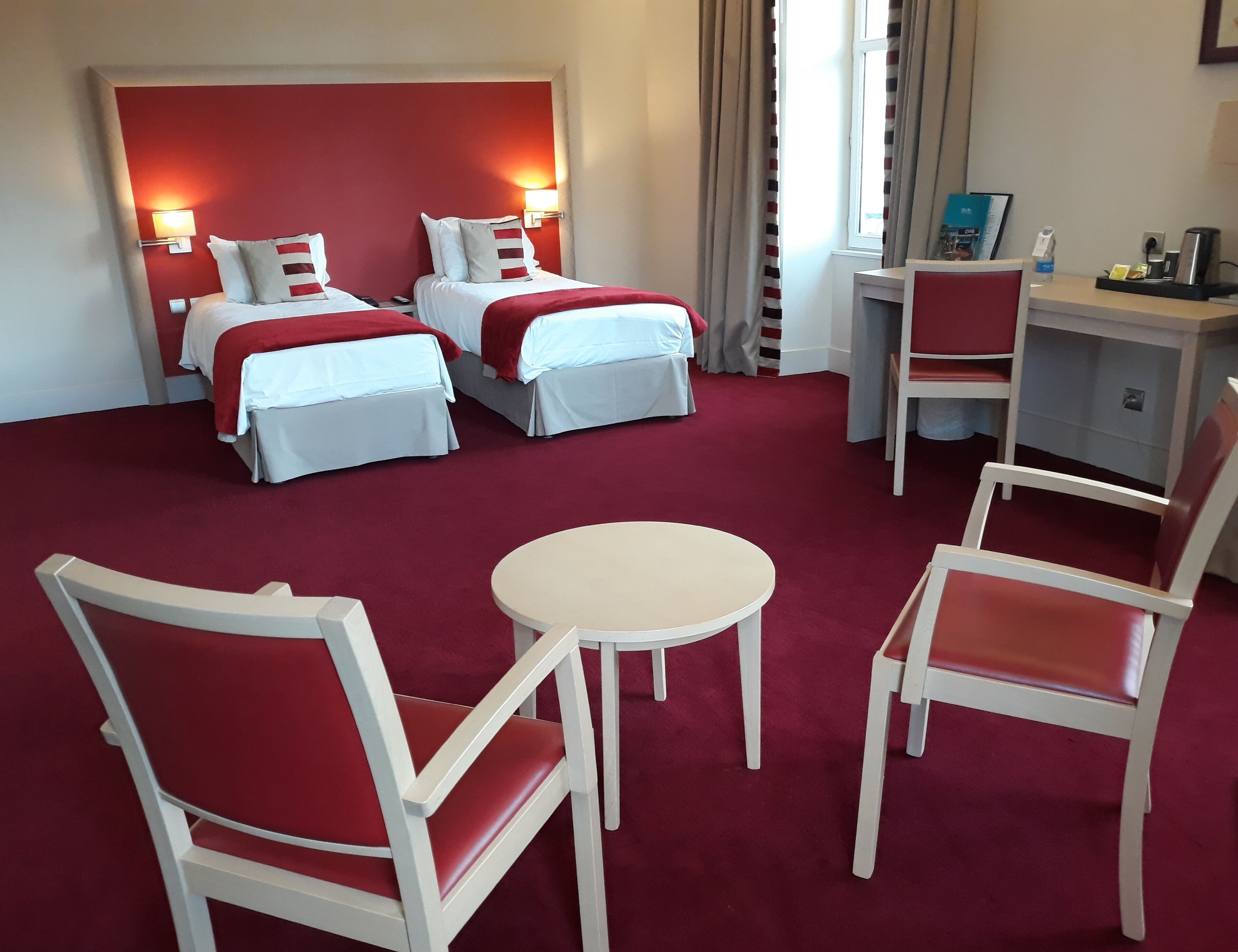 Habitación de hotel con dos camas, un escritorio, una silla y una mesita.