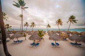 A beach with thatched umbrellas and lounge chairs, palm trees, and a calm sea. - Punta Cana Princess Adults Only - All Inclusive (Punta Cana)