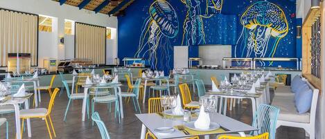A restaurant with colorful chairs and tables, a blue ceiling, and a mural of jellyfish on the wall.