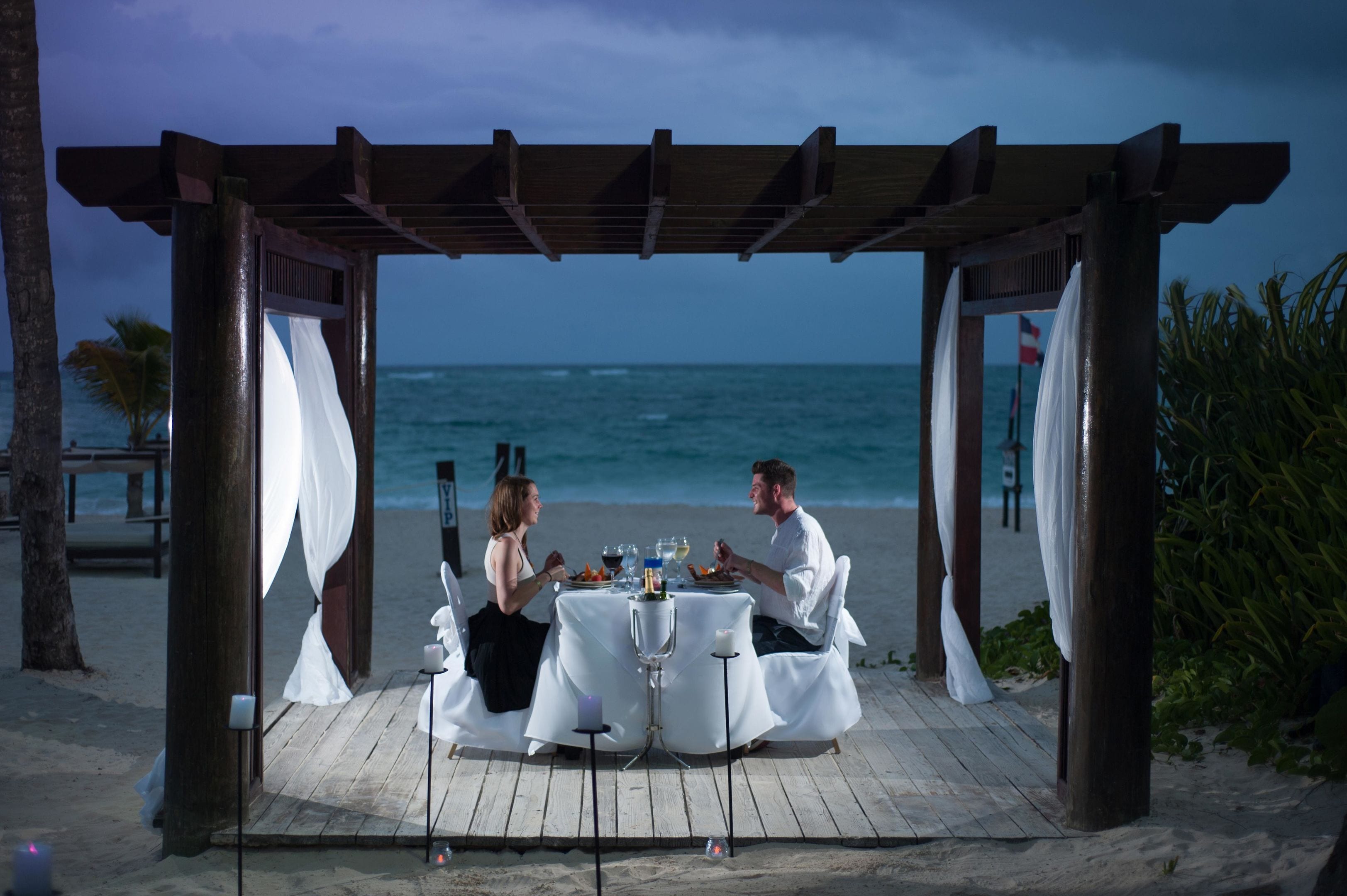 Una pergola in legno con tende bianche su una spiaggia.