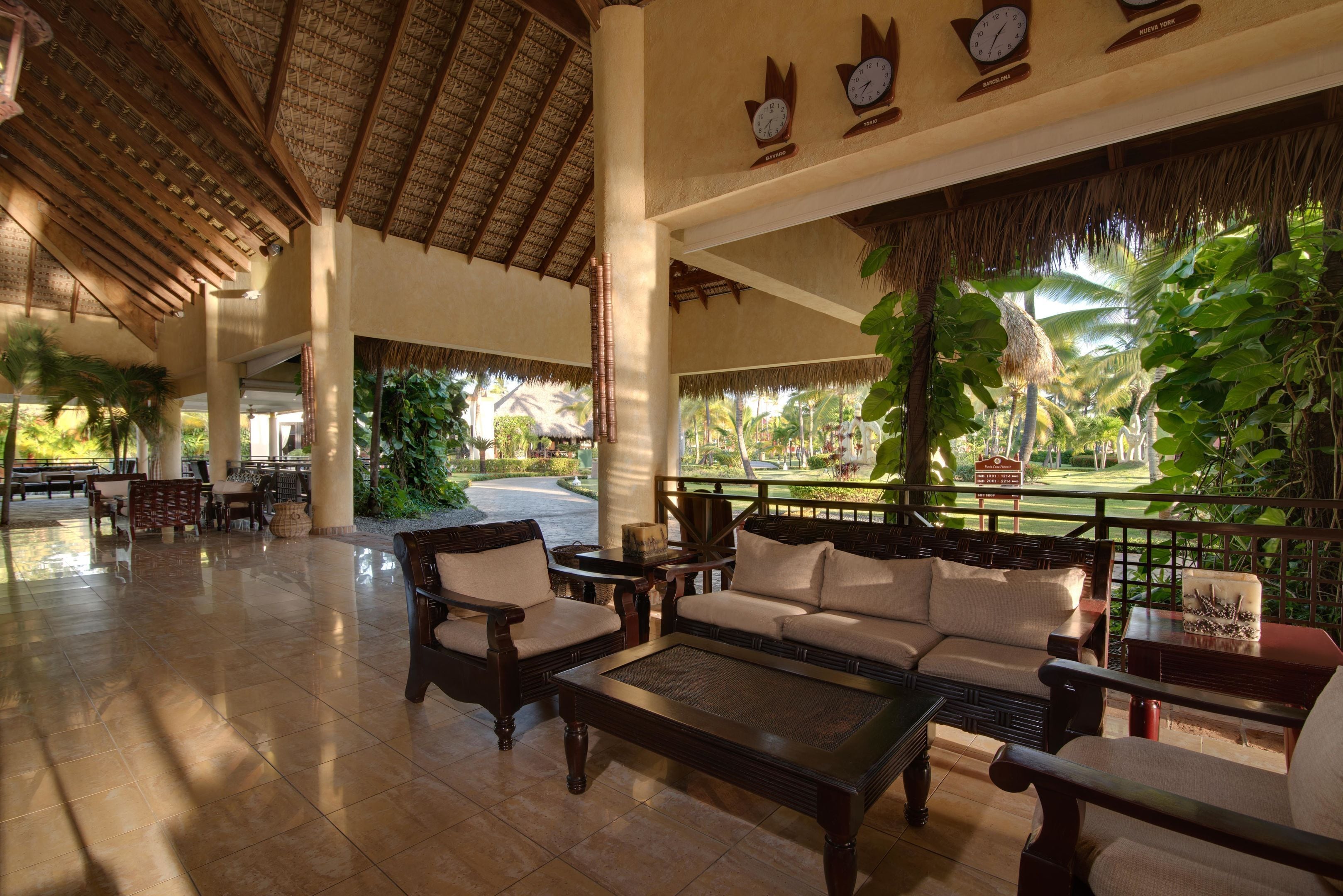 A spacious lobby with a high ceiling, wooden furniture, and a view of lush greenery outside.