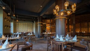 Un restaurant avec des tables et des chaises en bois, des luminaires suspendus et un mur en briques.